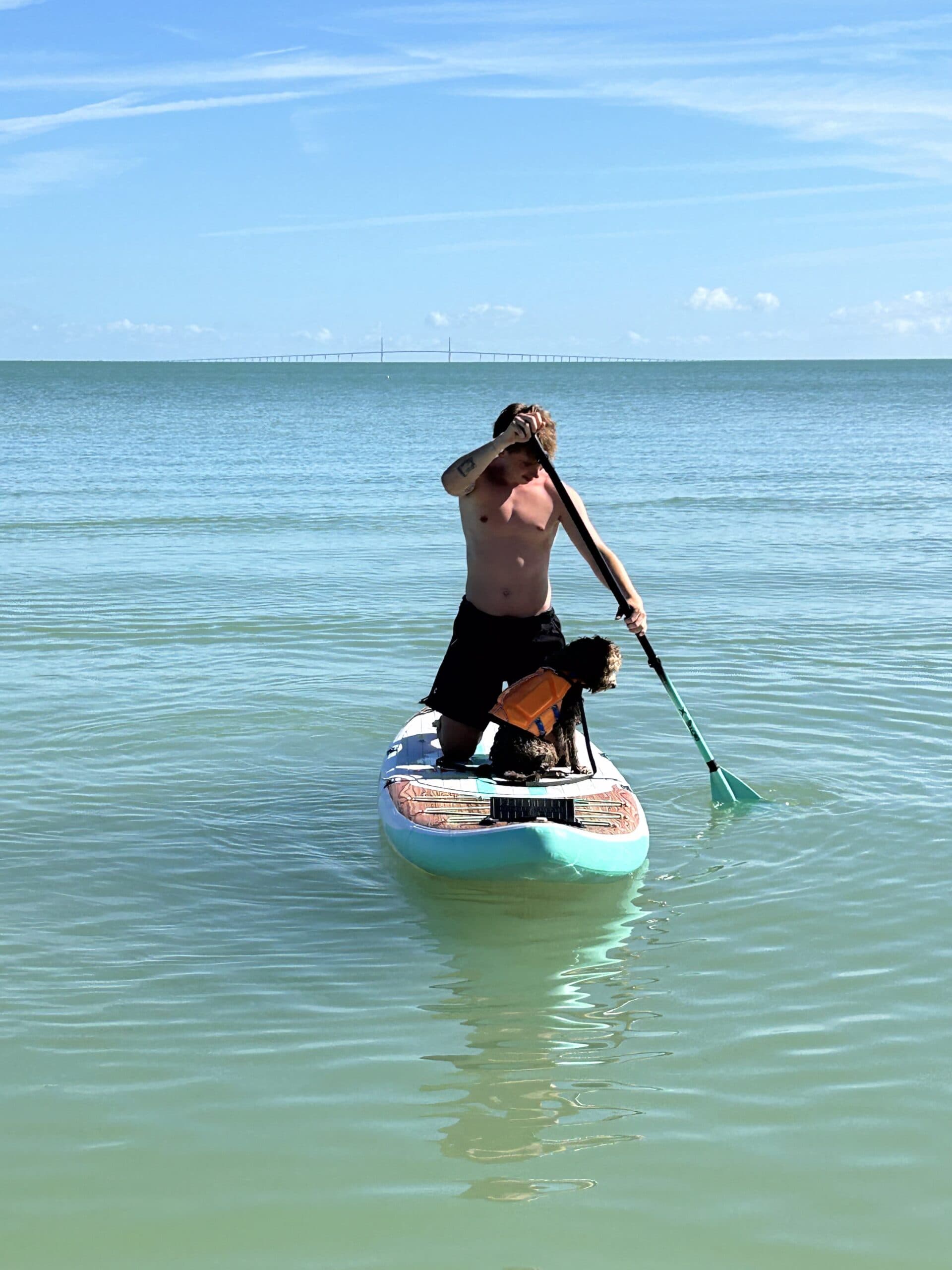 A man paddleboarding with his doodle